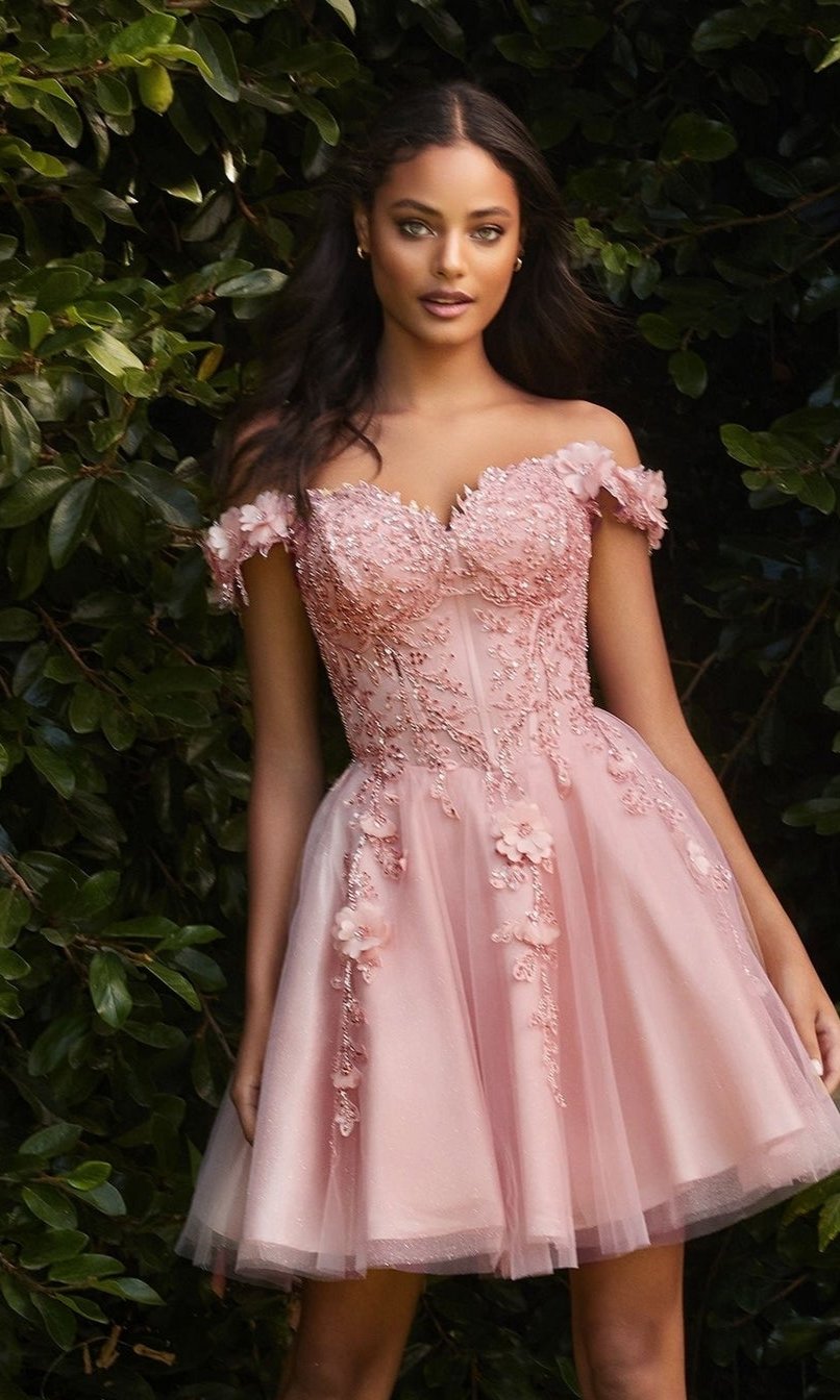 A woman stands outdoors before greenery, wearing the Off-Shoulder Short Floral Homecoming Dress CD0194—an a-line party dress in delicate pink with 3-D floral accents, an off-the-shoulder neckline, and a flowing tulle skirt.
